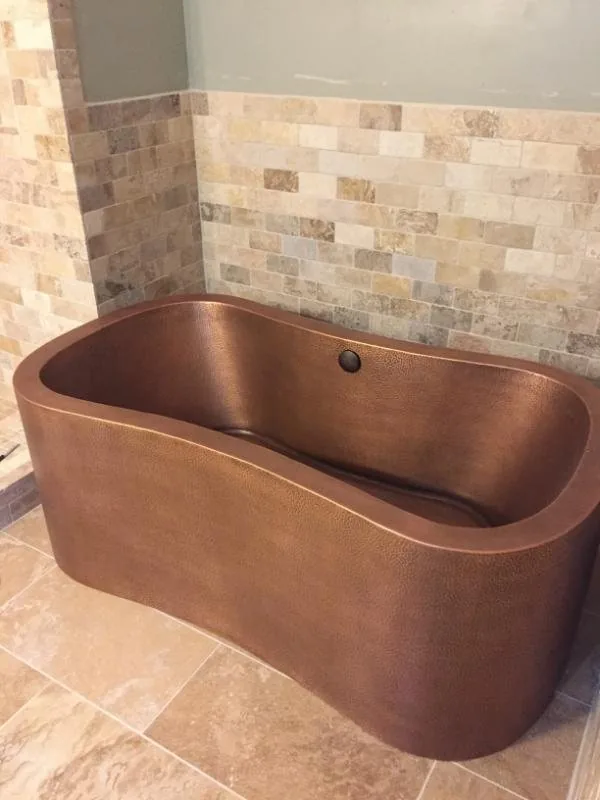 Copper soaking tub set against a travertine tile surround