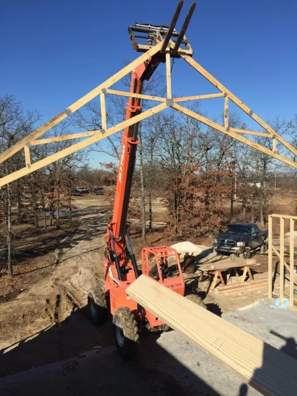 Crane lifting a roof truss into place over a new build site