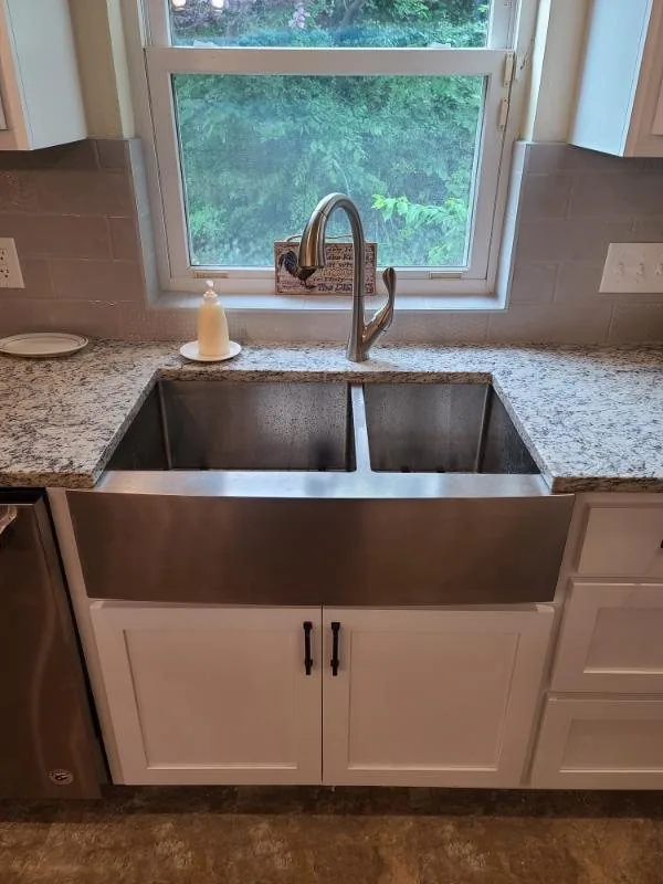 Copper farmhouse sink set into a granite counter under a window
