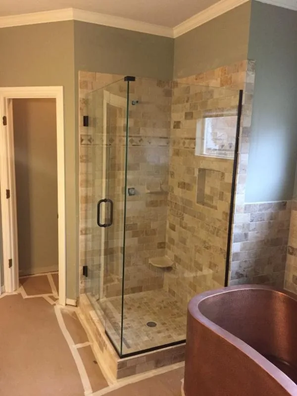Glass shower enclosure beside a copper soaking tub and stone tile